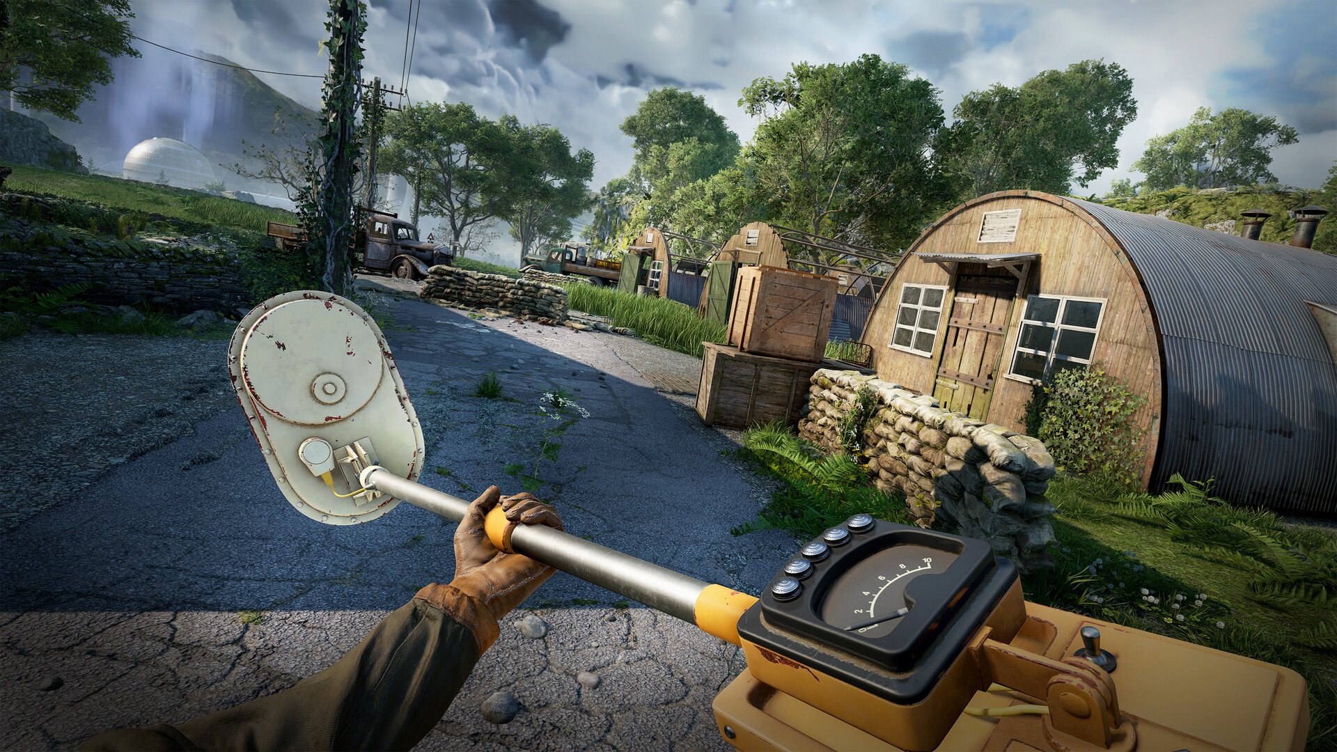 The player holds a handheld detector near a cluster of huts and abandoned vehicles.