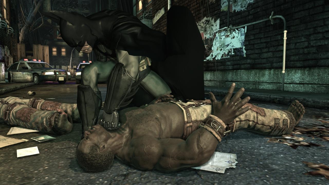 Batman pins a thug to the ground in a dark street.