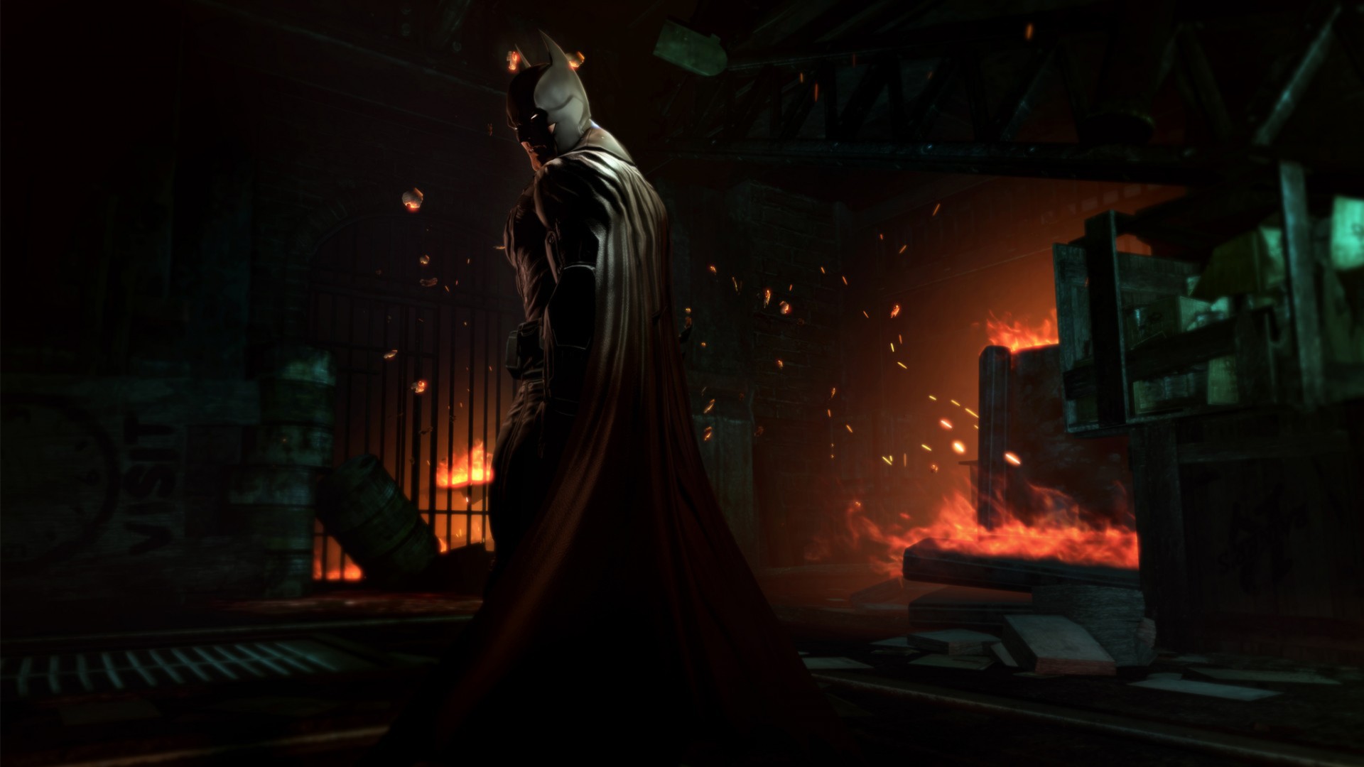 Batman walks through a dark industrial room lit by fire.