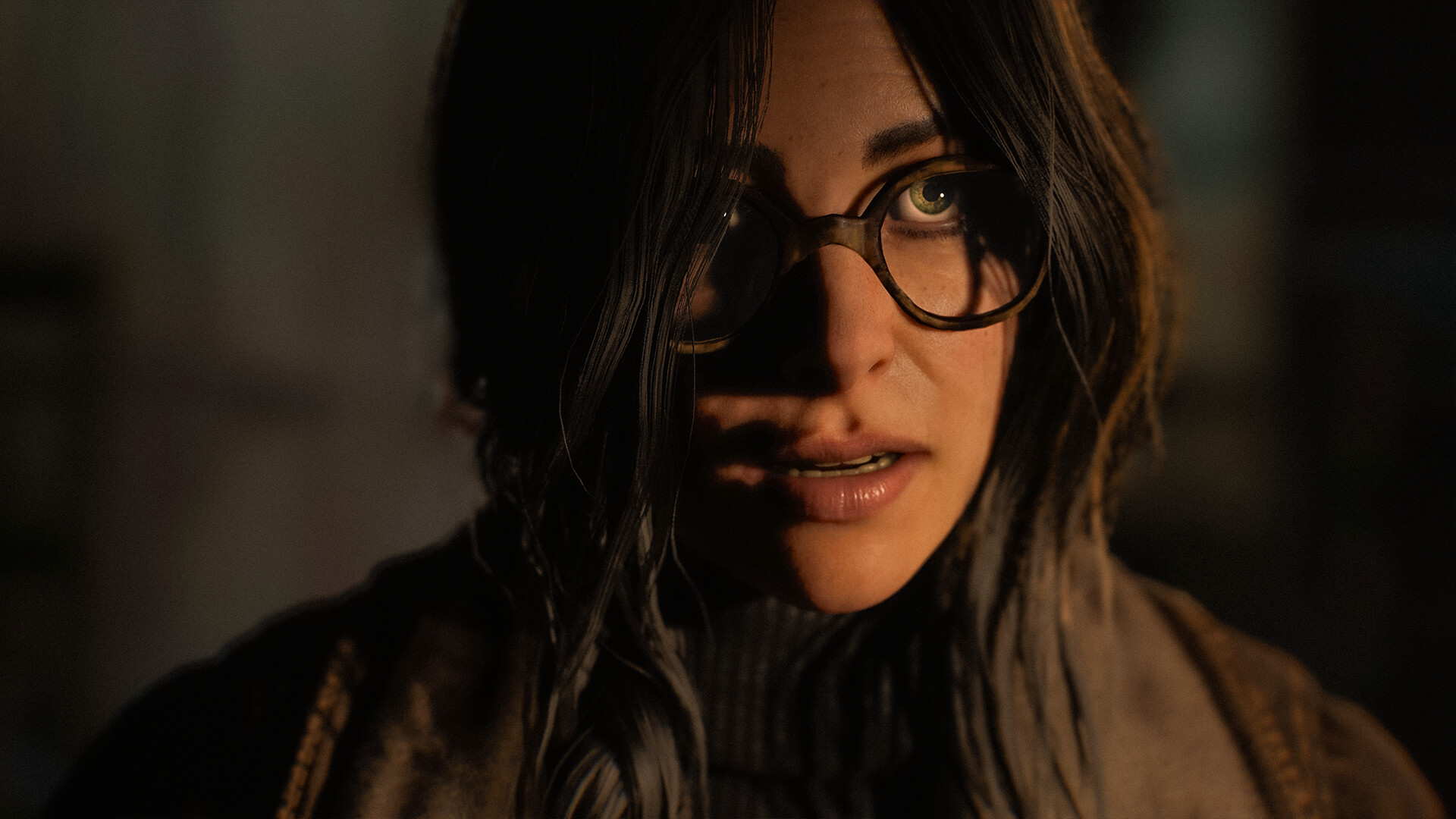 A woman with glasses appears in close-up against a dark background.