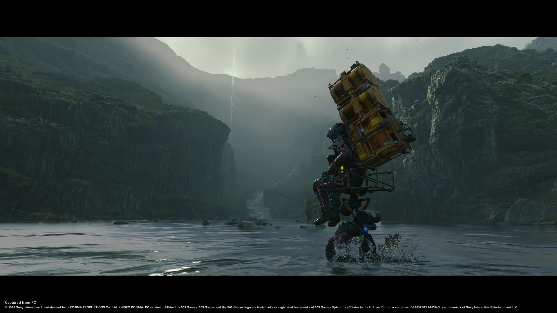 Sam crosses a rocky riverbed with cargo stacked on his back.