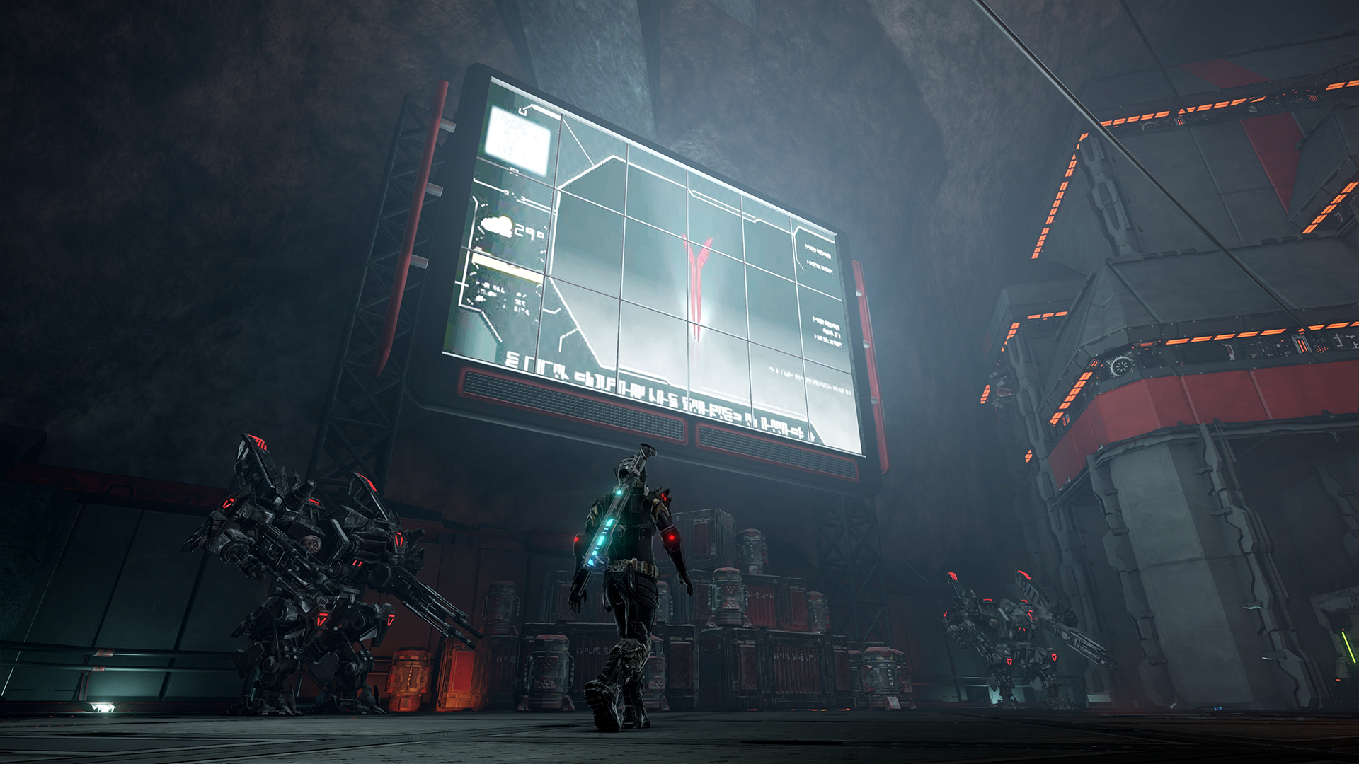 An armored figure stands beneath a large display in an industrial space.