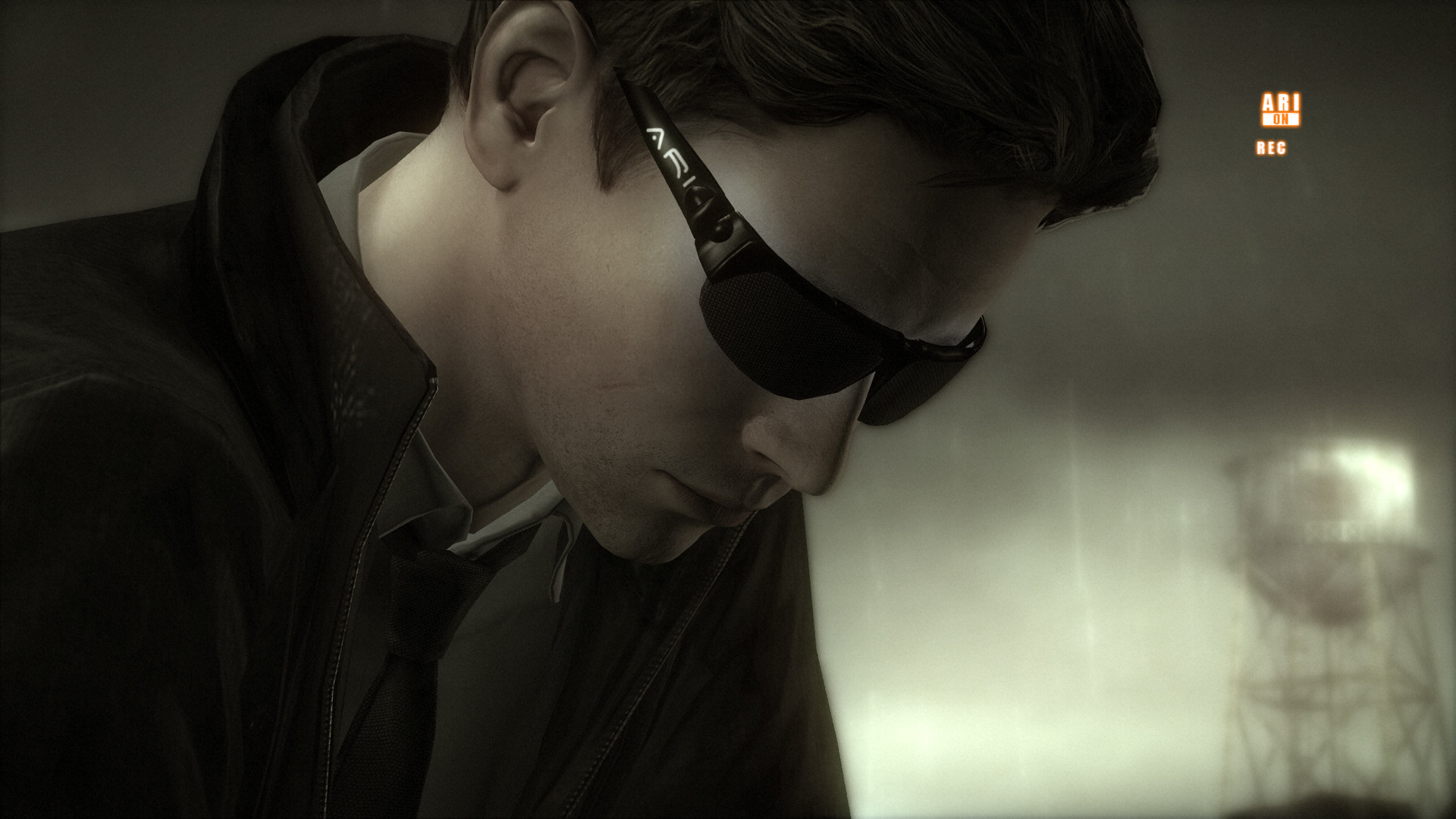 A man wearing dark glasses looks downward in a dim interior.