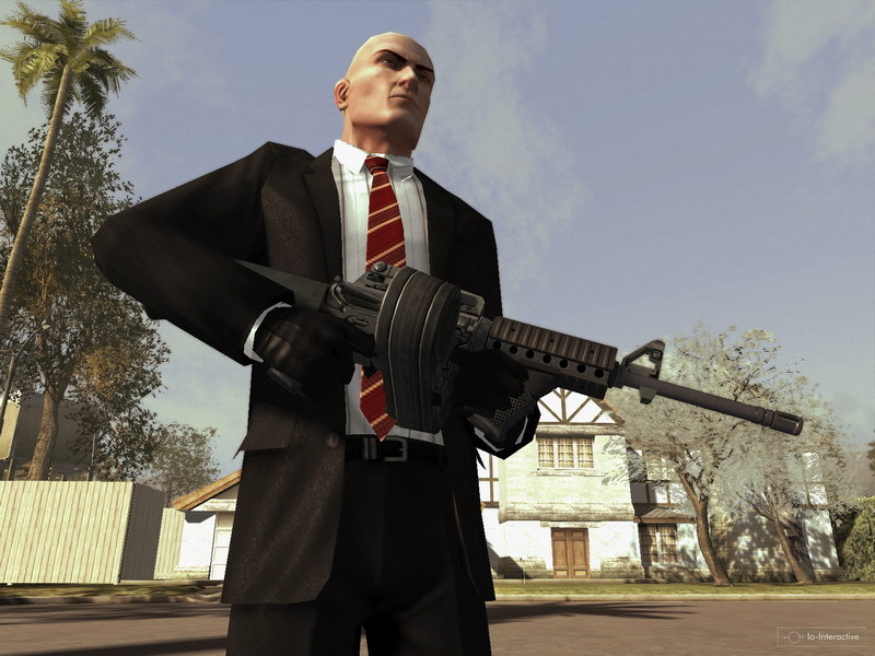 Agent 47 stands outdoors in a suit with a firearm.
