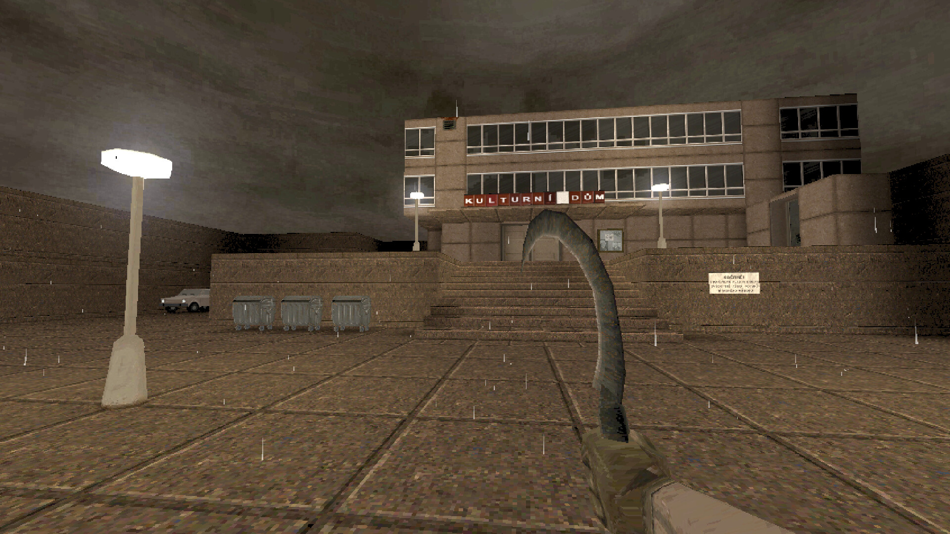 The player approaches a concrete building across a rainy square.