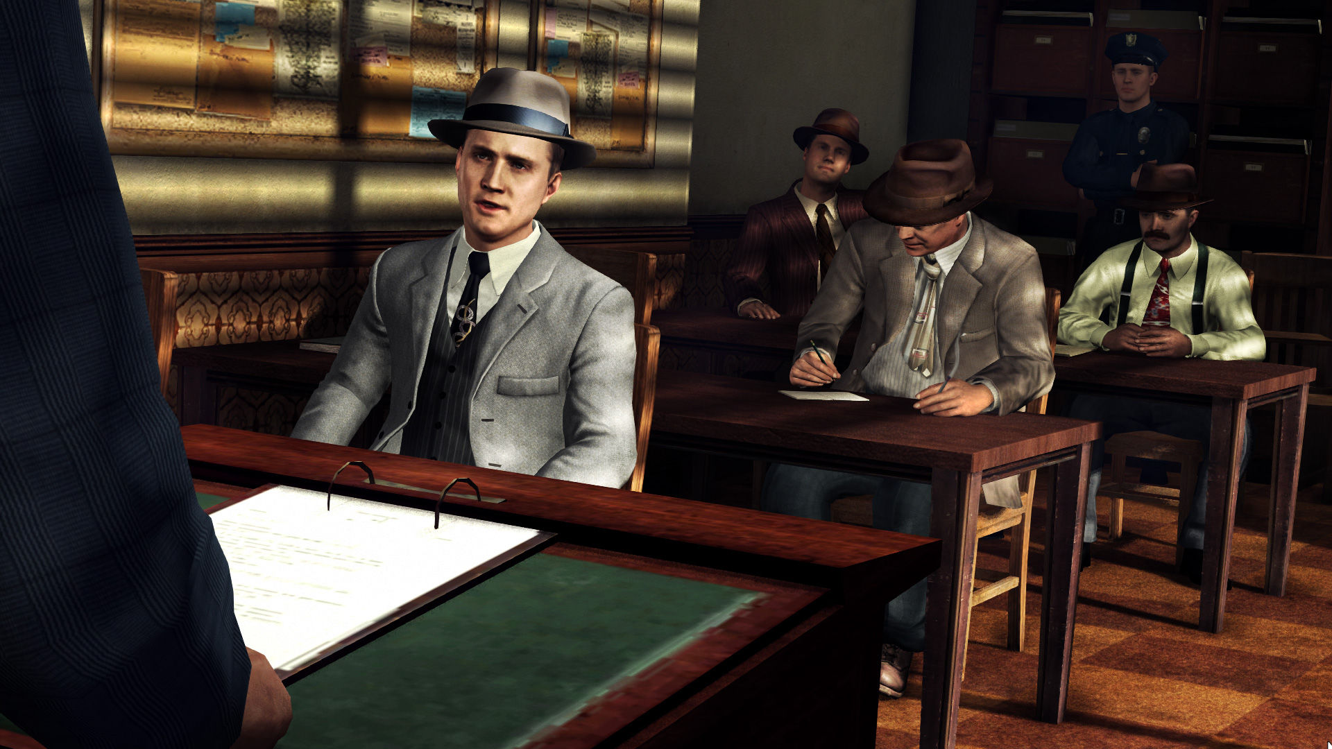 Cole sits across a table from a man in a formal room.