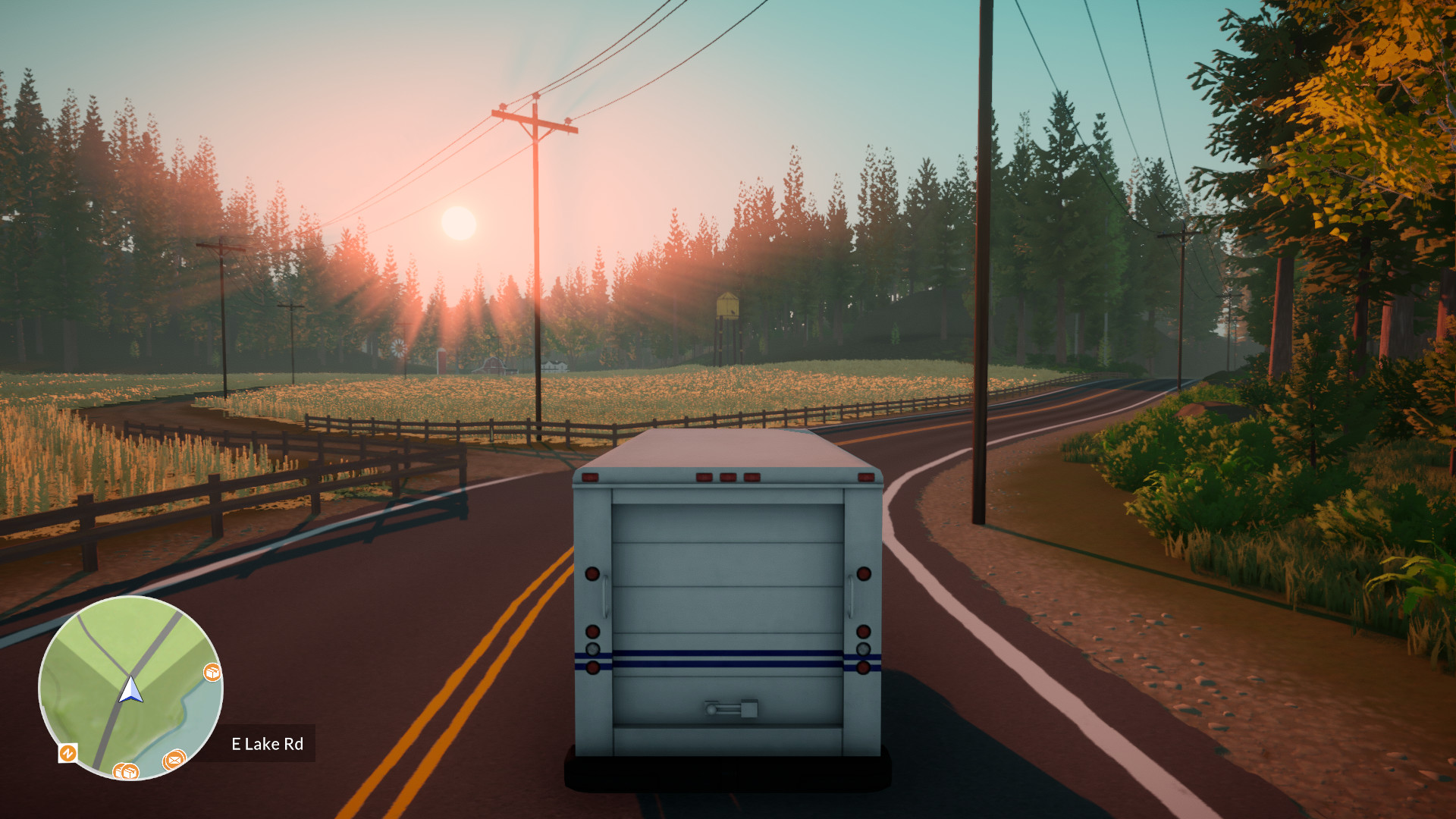 A mail truck follows a winding road through trees at sunset.