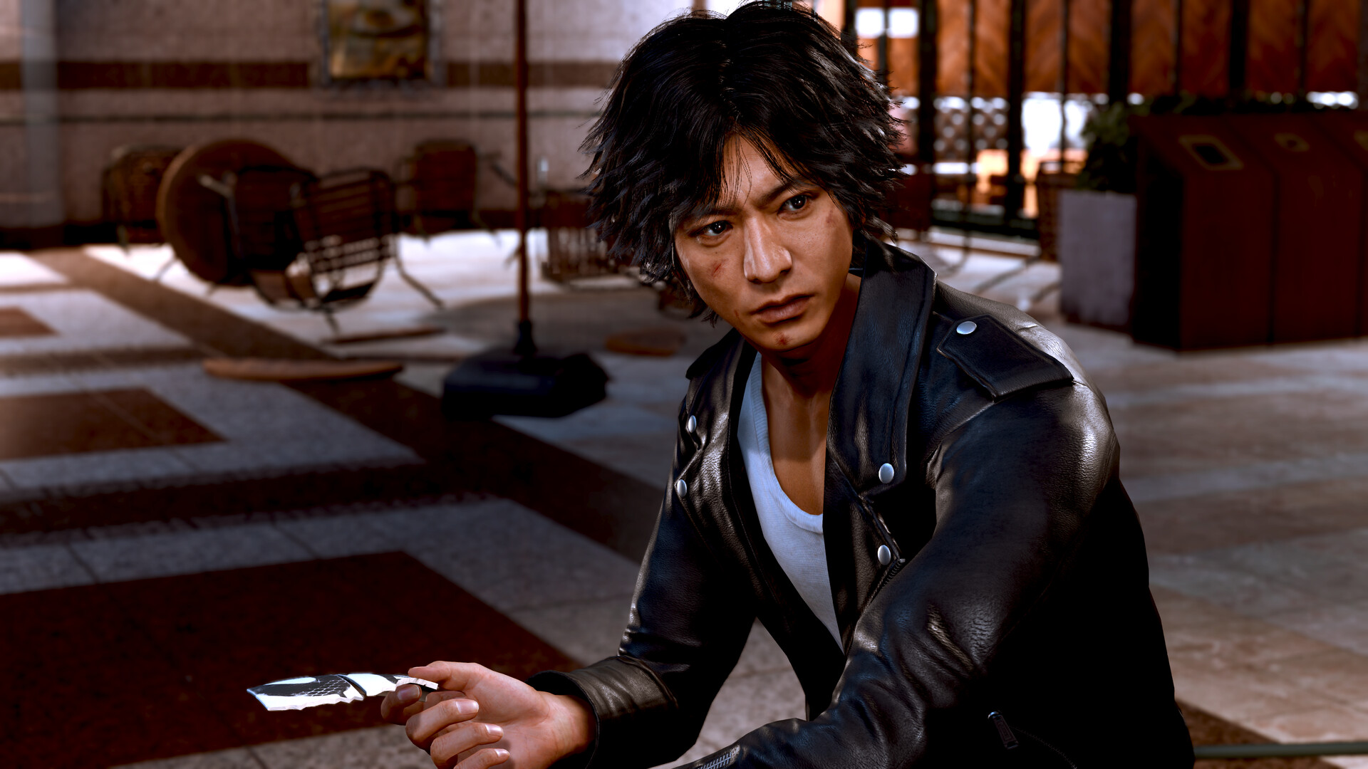 Yagami crouches with a phone in his hand.