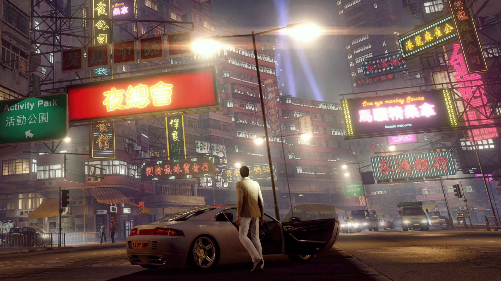A driver stands beside a car under Hong Kong street signs at night.