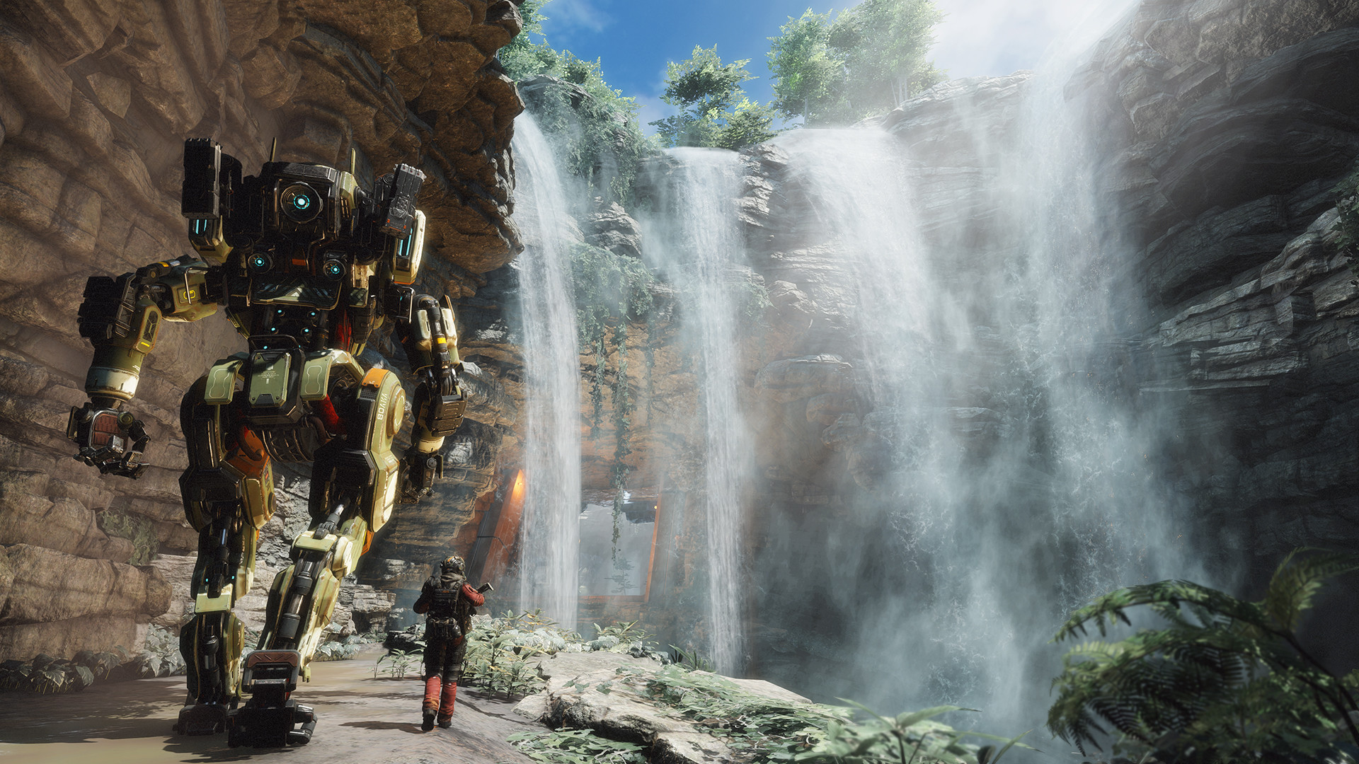 A pilot stands beside a Titan near a waterfall.