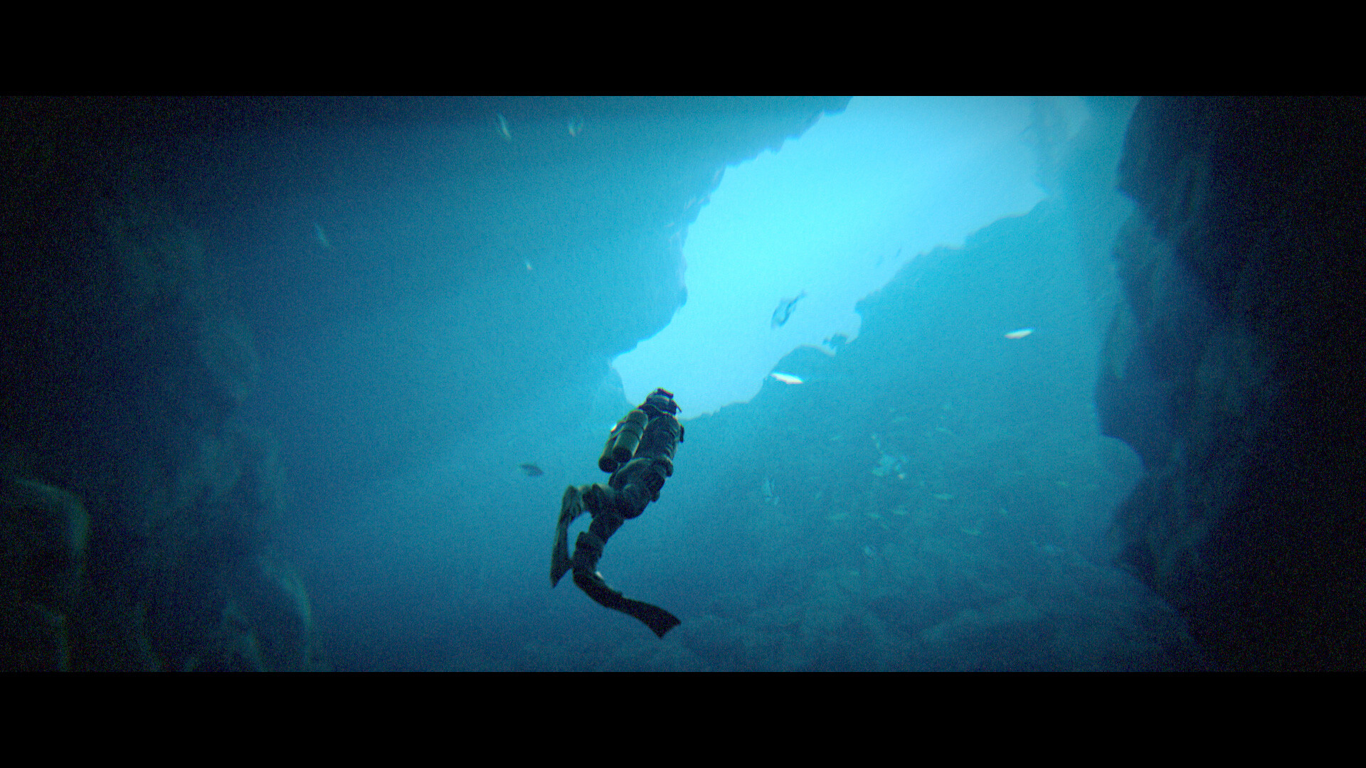 A diver swims upward between steep walls of a blue underwater passage.